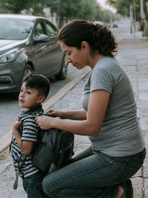 Mamá ajustando la mochila de su hijo en la banqueta antes de salir